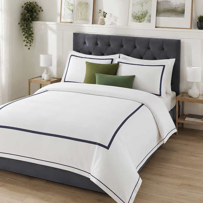 White hotel style bedding with a navy satin stitch border, matching bordered pillowcases and green accent cushions.