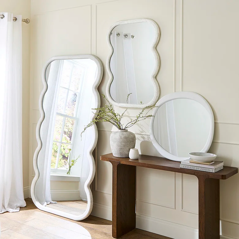 three white mirrors around a wooden console table