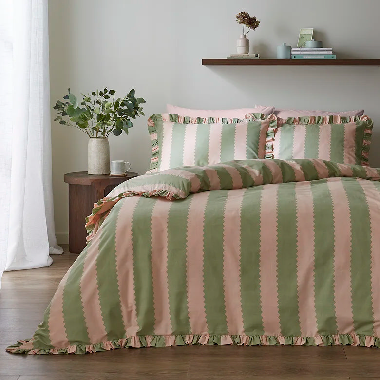 pink and sage green striped duvet cover set with ruffle trim styled in soft neutral bedroom with wooden furniture and natural accents