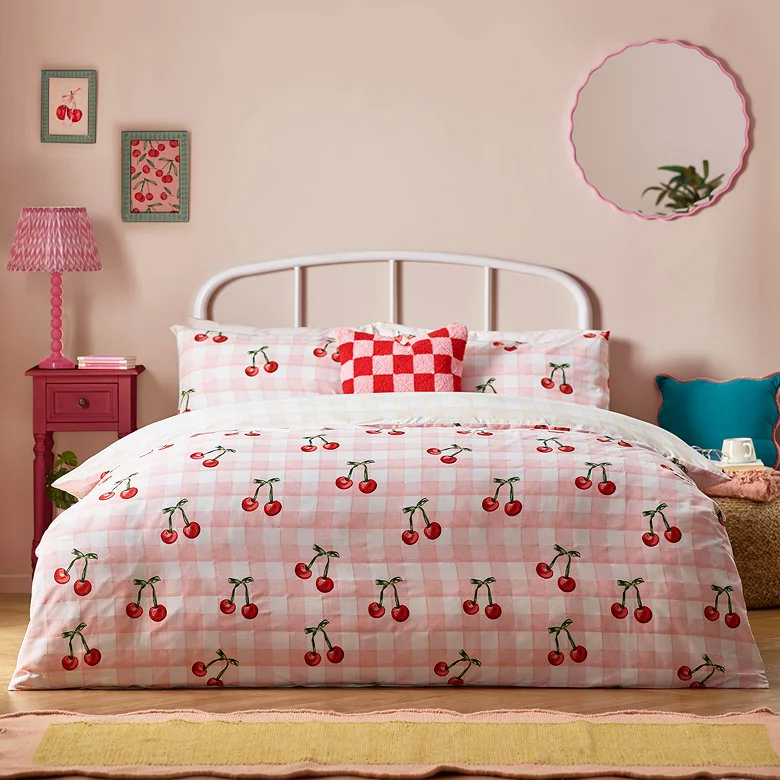 pink gingham cherry print duvet cover set styled in playful bedroom with bold cushions and colourful retro decor