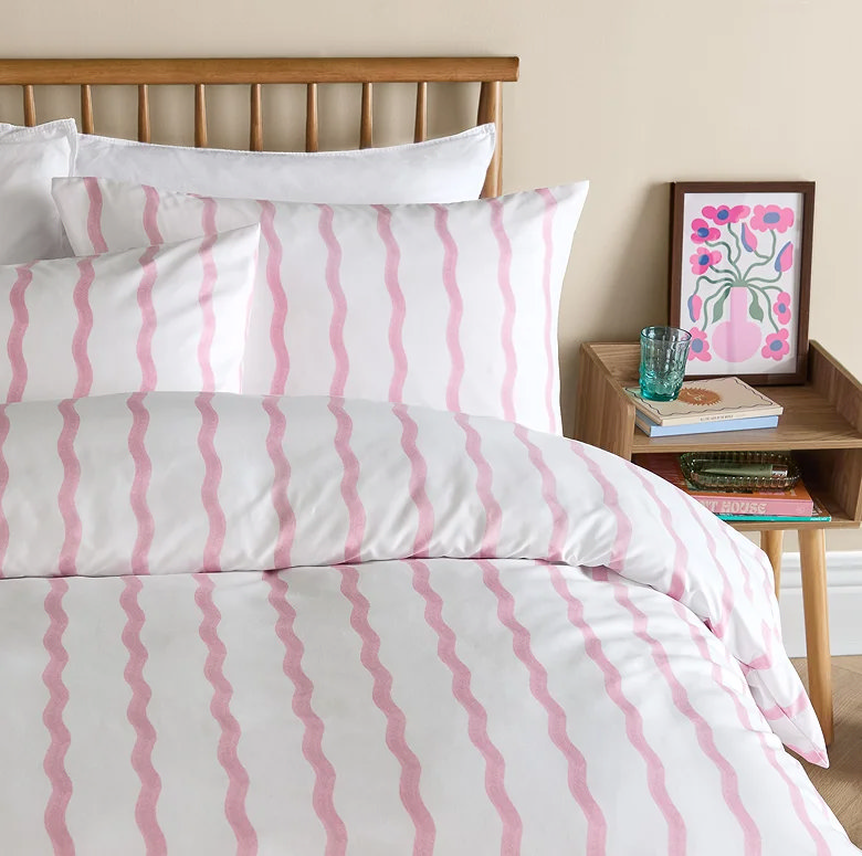 white duvet cover set with soft pink wavy stripe pattern styled in modern bedroom with wooden bedside table and simple decor