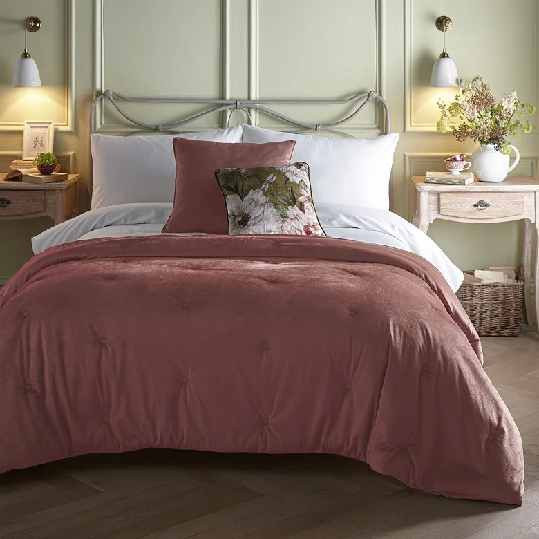 dusty pink velvet quilted bedspread styled with white bedding on metal frame bed