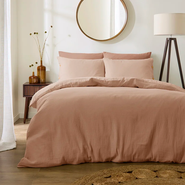 warm peach pink muslin duvet cover set with soft textured finish styled in neutral bedroom with wooden furniture and round mirror