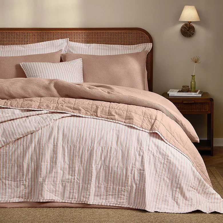 blush pink striped quilted bedspread with matching stripe bedding on rattan headboard bed