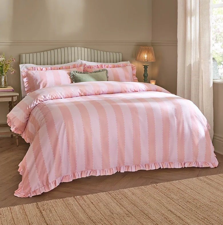 pink striped duvet cover set with ruffle trim styled in cosy bedroom with warm lighting and neutral decor