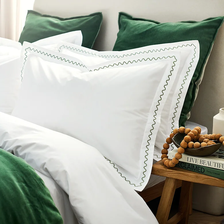 white bedding with green embroidered trim pillowcases and velvet cushions in modern bedroom