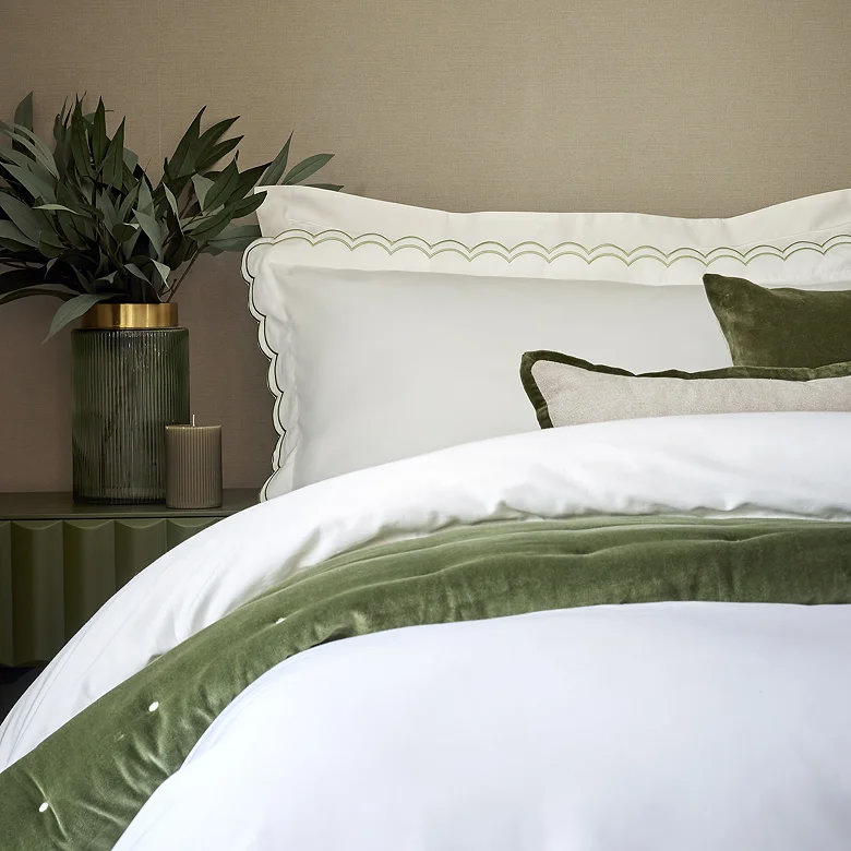 white bedding with green scalloped edge trim and velvet throw in neutral bedroom