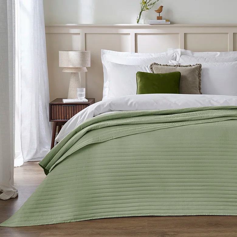 sage green quilted bedspread with white bedding and layered cushions in calm neutral bedroom