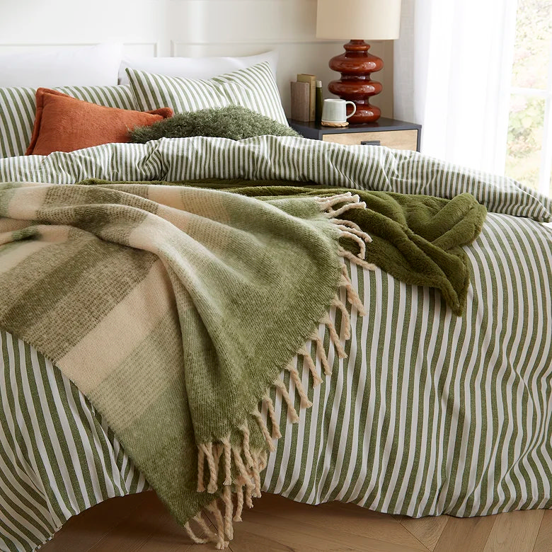 green striped duvet cover set with layered throws and cushions in cosy bedroom