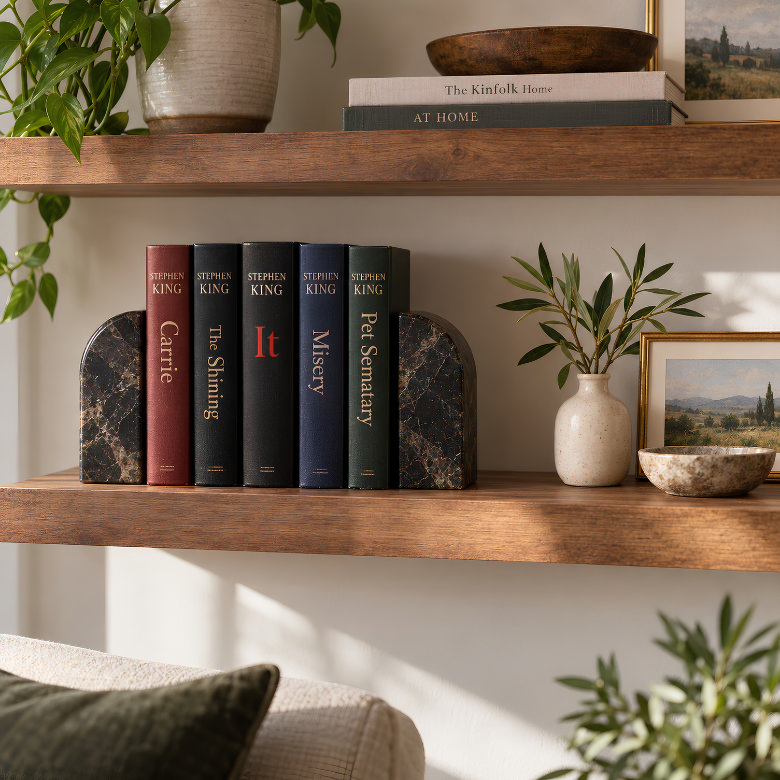 Books by the same author grouped together between bookends on a wooden shelf with plants and decorative accessories