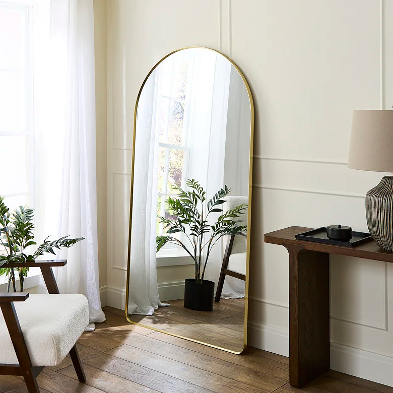 large arched golden freestanding mirror with faux plant
