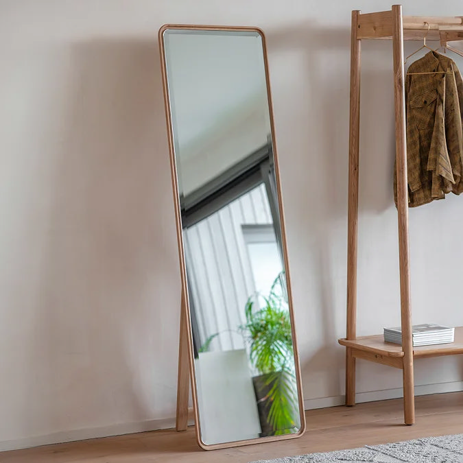 Minimalist rectangular floor mirror with slim oak frame, freestanding in a modern living room corner to reflect light and add height.