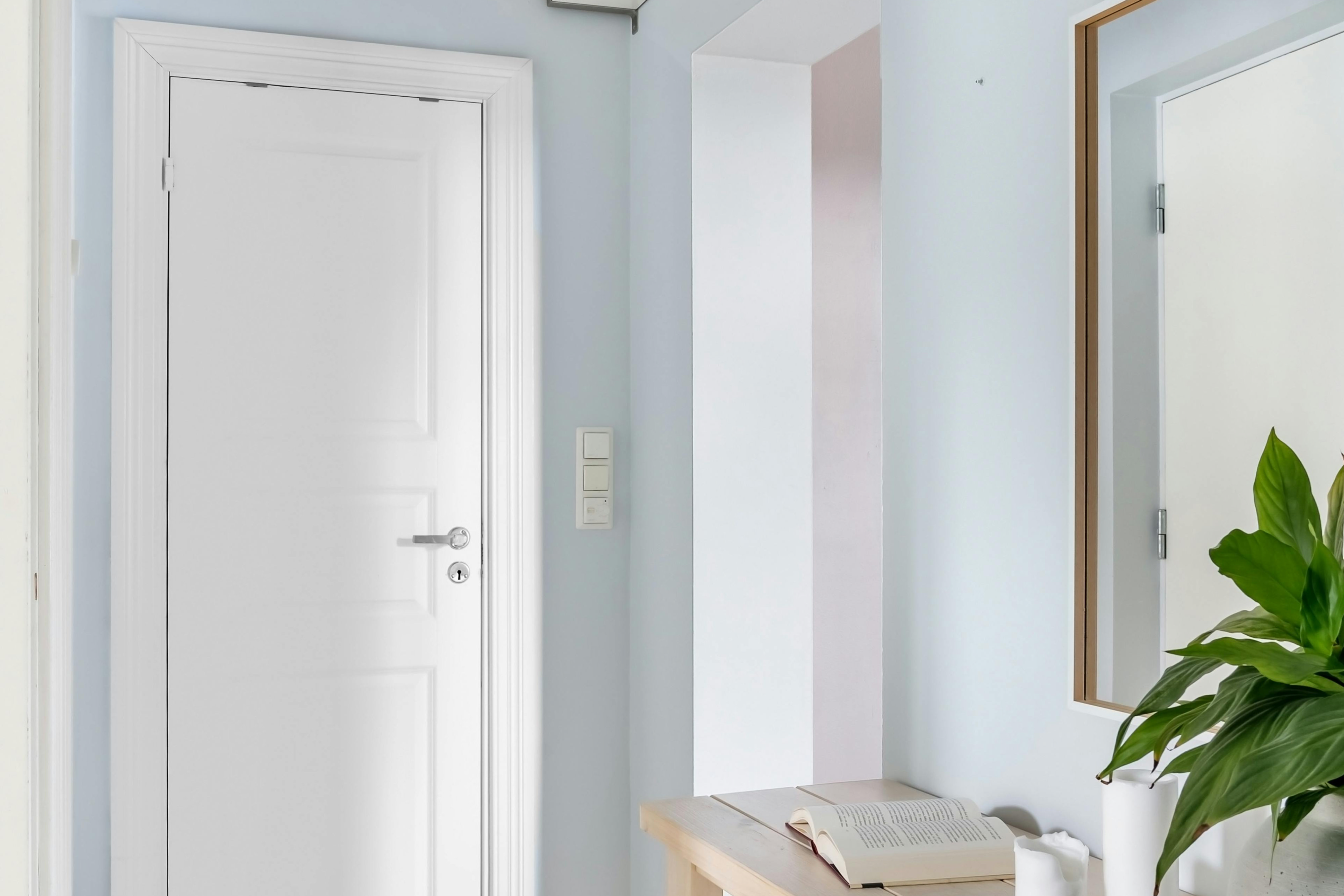 Small hallway painted in cool blue-grey with white door and trim, slim console, plant and mirror — showing how receding hues make a narrow hall look wider