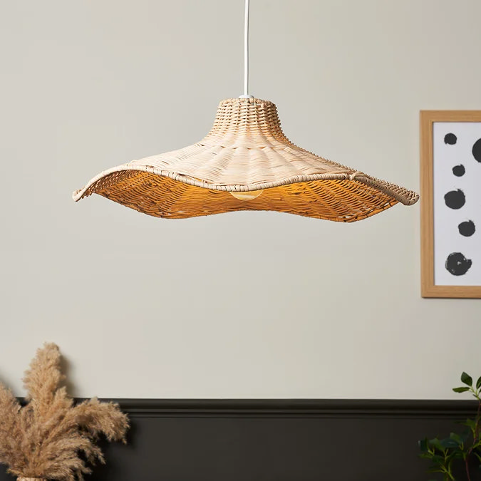 Curved woven rattan pendant light with organic, wave-like shape, suspended over a neutral dining space with black panelling, pampas grass, and modern monochrome wall art.