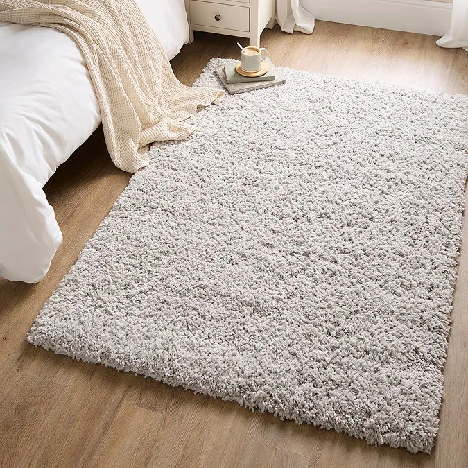 Light grey shaggy rug beside a bed on wooden flooring to add warmth and comfort in winter