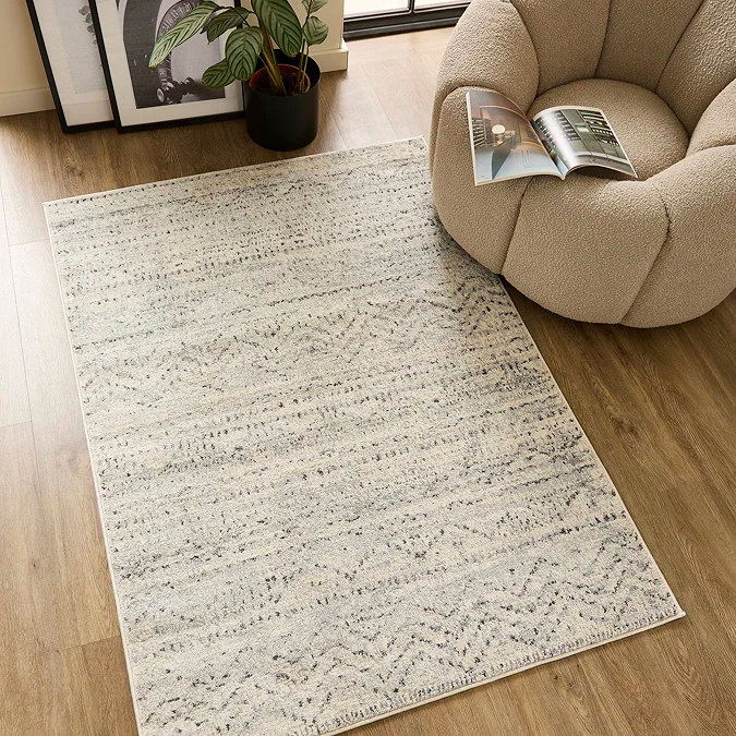 Light grey patterned rug with a soft, low-pile finish, styled beside a boucle accent chair and indoor plant on wooden flooring — a calm, modern office rug idea that reduces visual noise and creates a focused, professional work zone at home