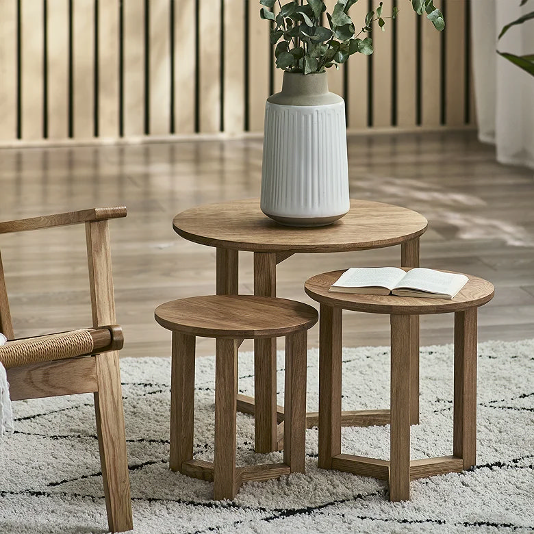Wooden nesting tables styled with vase and open book as tiered book storage idea for small spaces