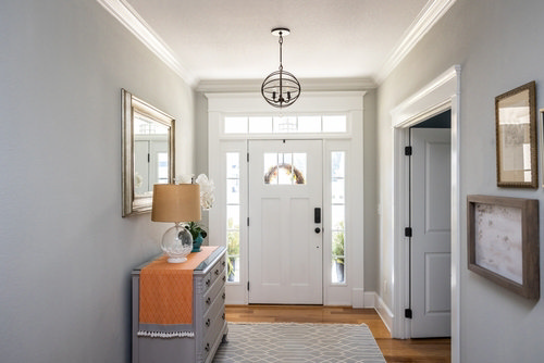 Bright narrow hallway with glazed front door, transom and sidelights, mirror and console, pale grey walls and patterned runner—widening the space. 