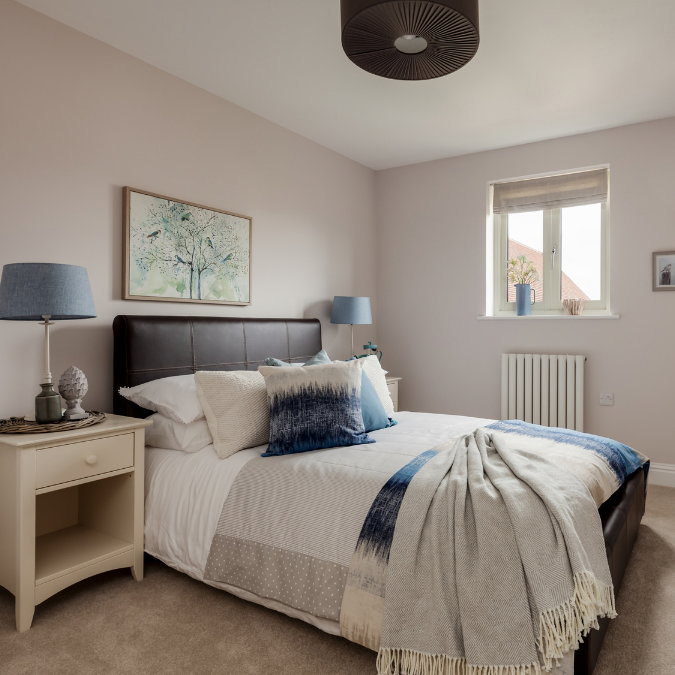 Modern bedroom with clear radiator space, bed dressed in layered throws and blue cushions