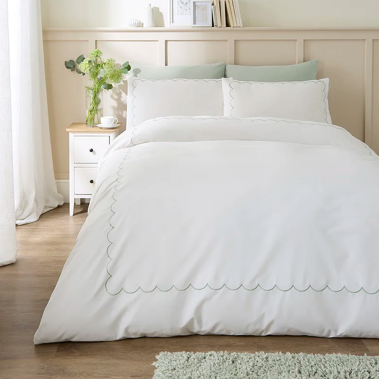 Light bedroom with white scalloped bedding and soft sage accents.