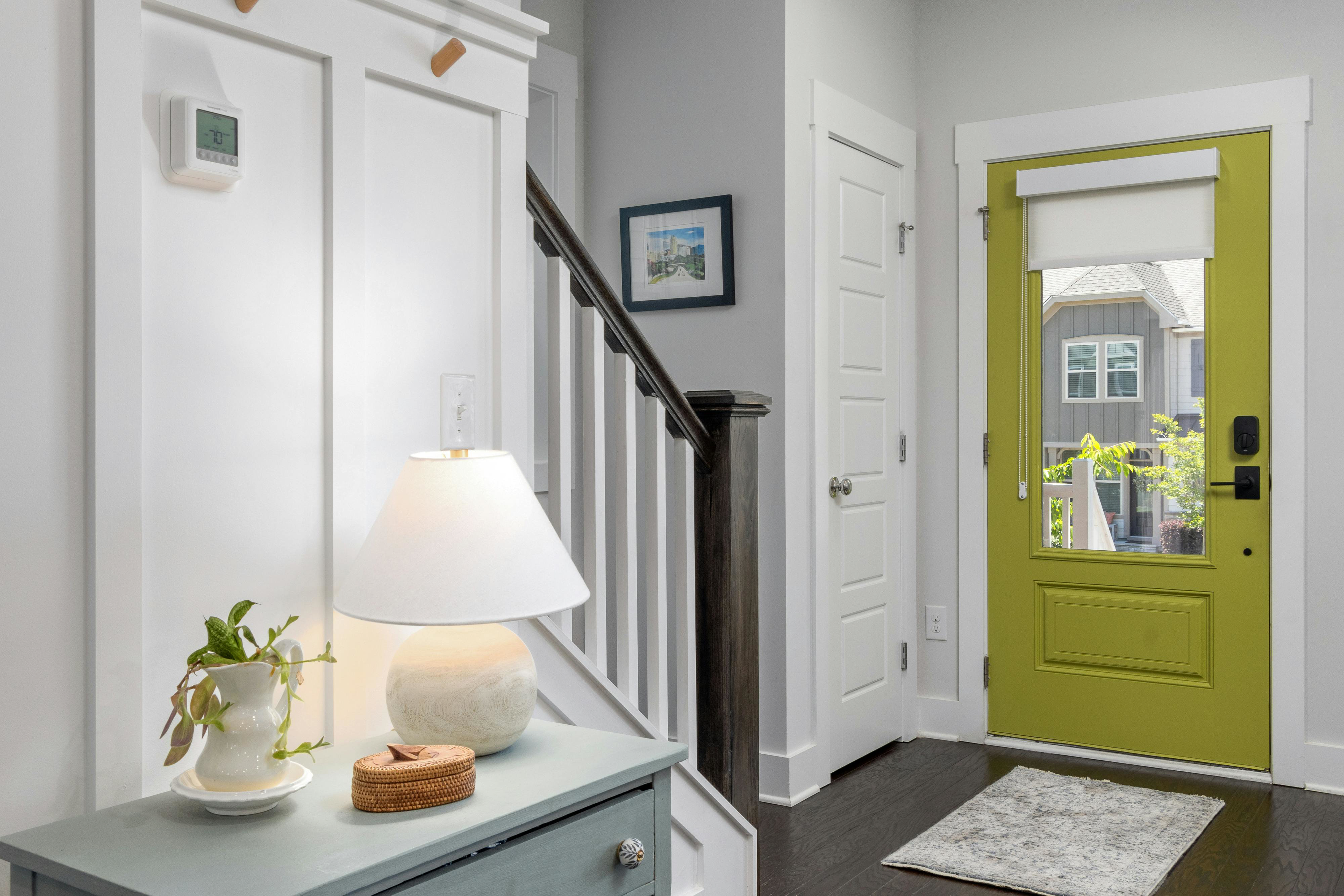 Bright entryway with chartreuse front door and glass panel, white walls, console lamp and staircase—natural light making a narrow hallway feel wider.