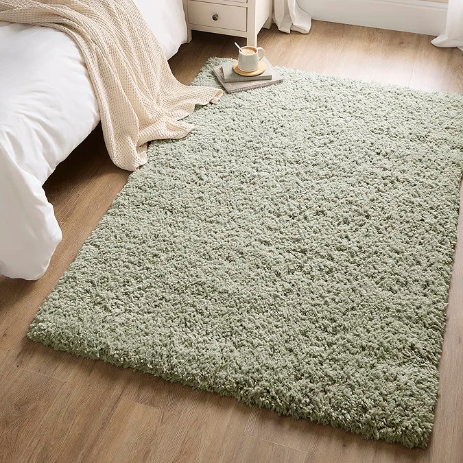 Soft sage green shaggy rug on a wood floor beside a bed and cream throw, showing how choosing a rug in your favourite colour can personalise a home office or WFH nook with warmth and comfort