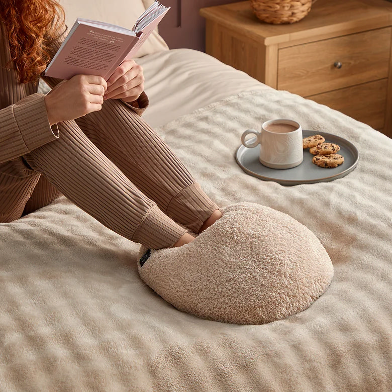 Person relaxing on bed reading with soft fleece foot warmer cushion