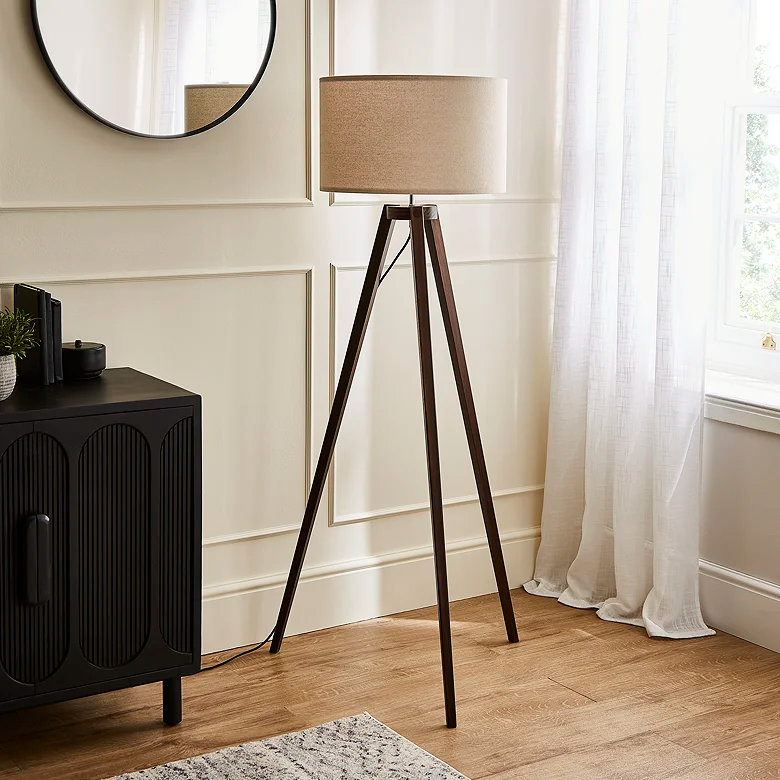 Dark wood tripod floor lamp with beige fabric drum shade beside window in living room
