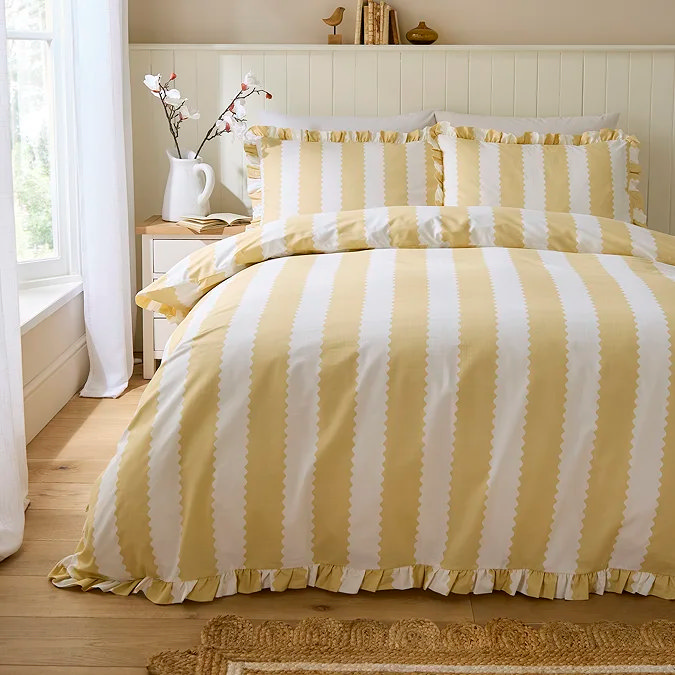 Butter yellow striped duvet cover with ruffled bedding in neutral bedroom.