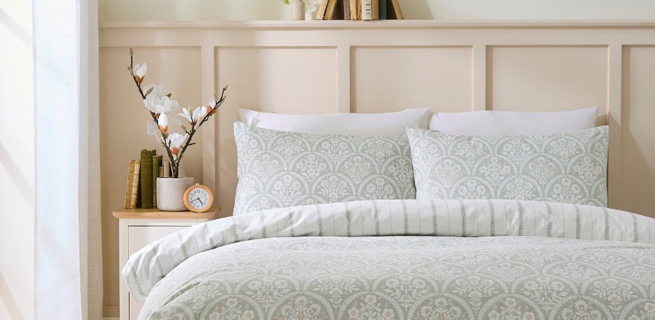 Bright bedroom with sage-patterned bedding, magnolia stems on the nightstand, and morning light streaming in for fresh airflow.