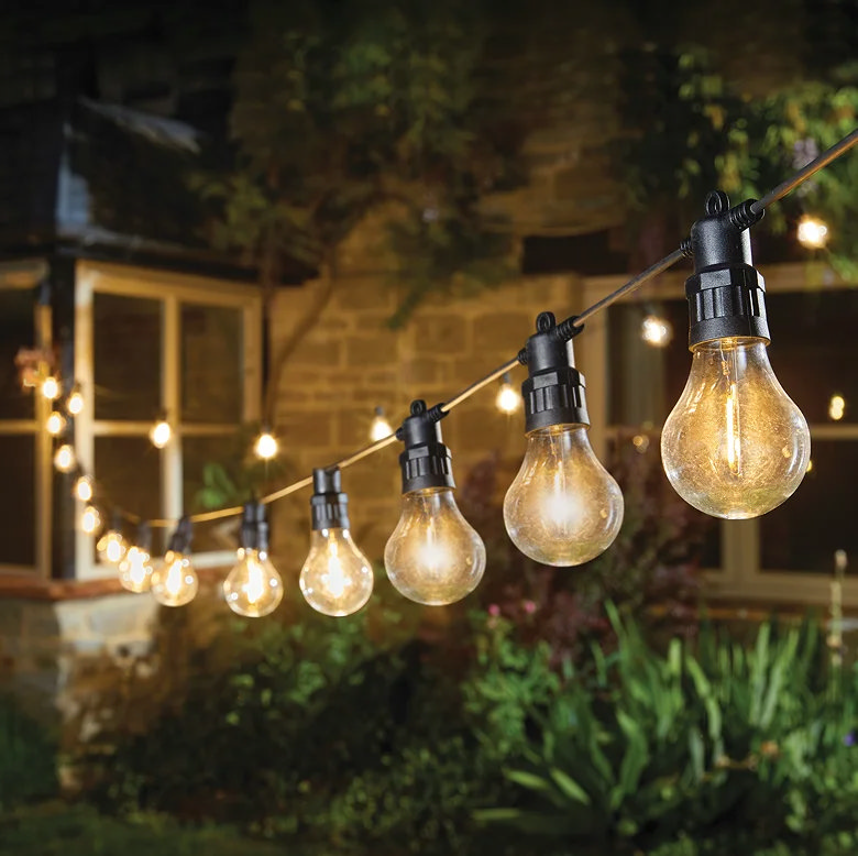 Warm white festoon string lights hanging across a garden patio creating cosy outdoor evening lighting