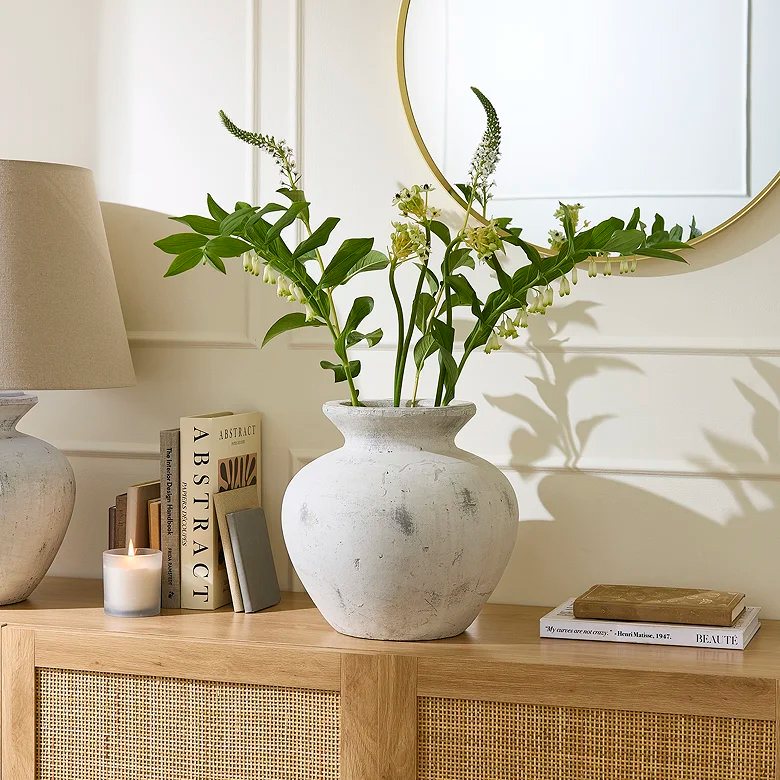 Large ceramic vase with green stems styled on wooden sideboard