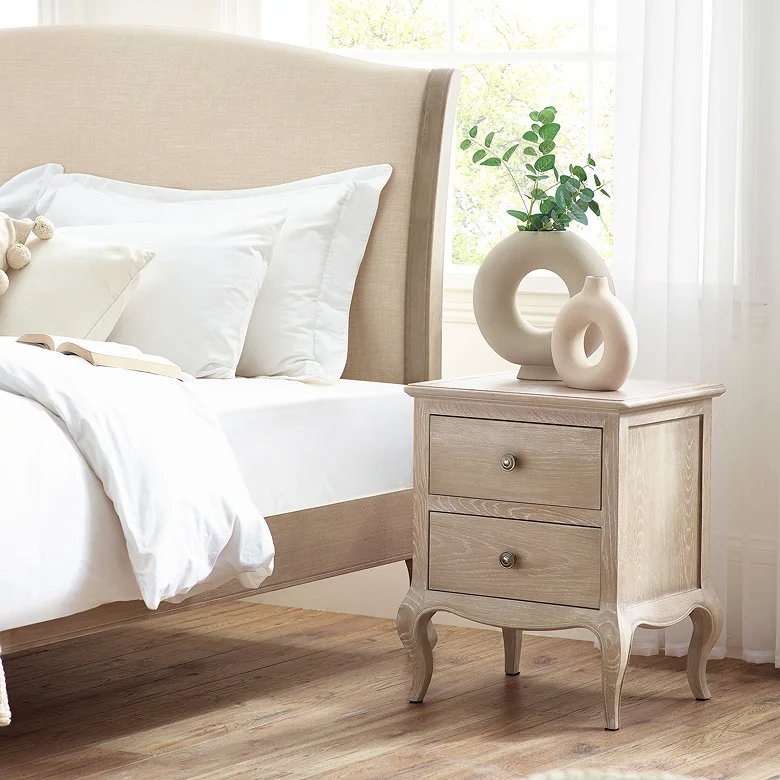 bedroom with light wood two drawer bedside table and curved legs beside upholstered bed