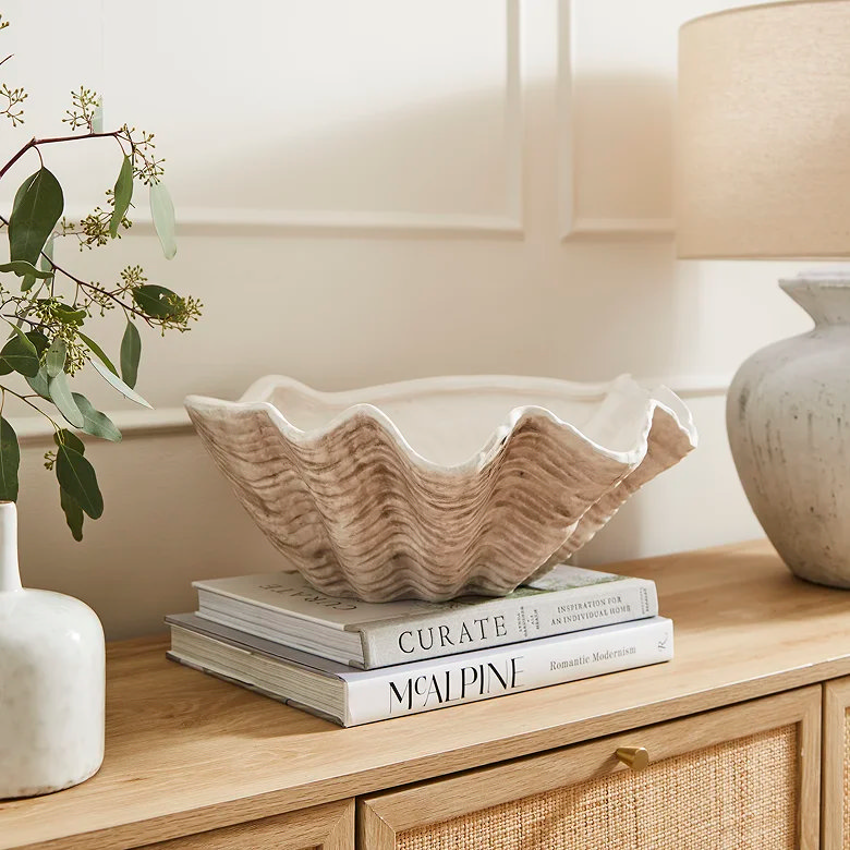 Decorative ceramic shell bowl styled on stacked books on wooden sideboard