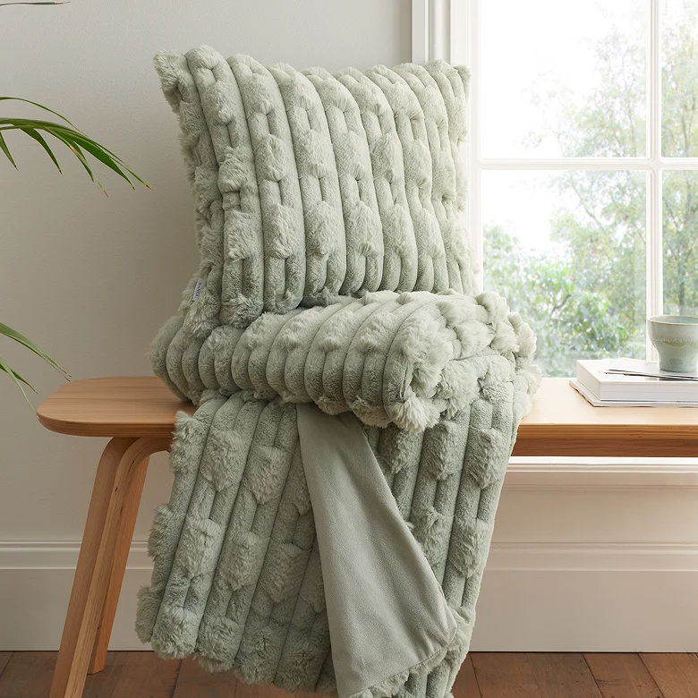 Sage green carved faux fur throw draped over a wooden bench by a window
