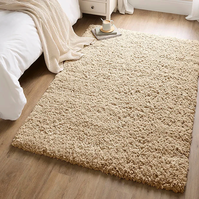Cosy beige shaggy rug on wooden floor beside a bed, showing how a plush neutral rug can warm a minimalist home office or desk nook, add softness underfoot, and zone a workspace in a shared room