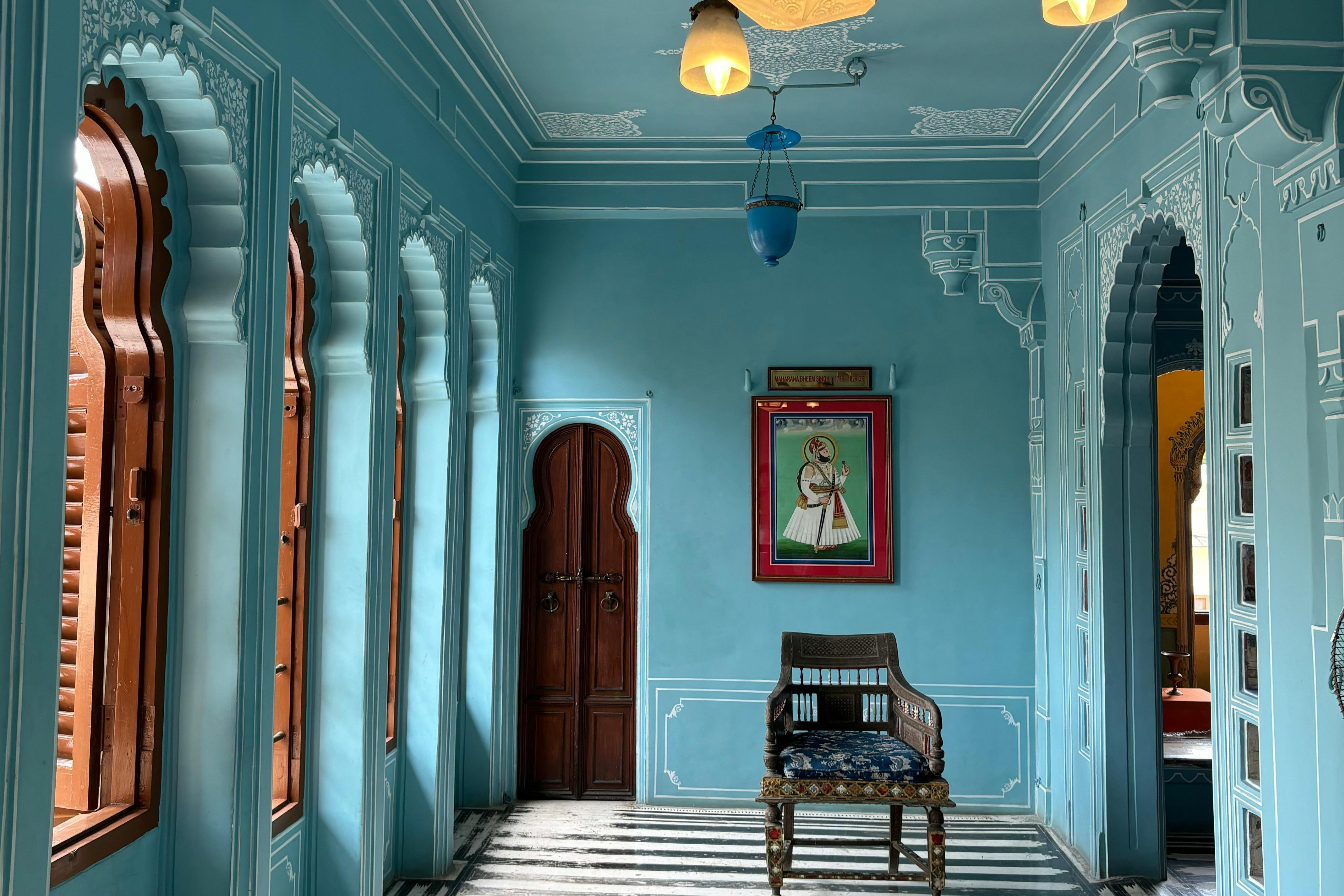 Colour-drenched hallway — walls, ceiling and trim all turquoise with arched windows and a striped floor — showing how one mid-tone makes a narrow corridor feel wider.