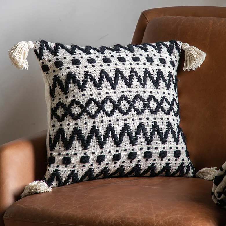 Black and cream patterned cushion with tassels on brown leather chair