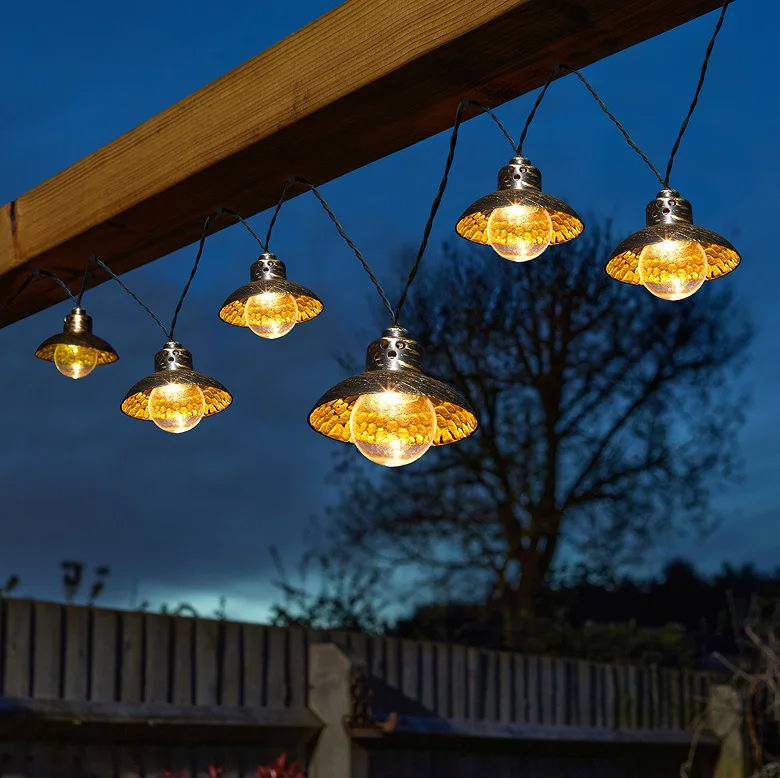 Outdoor string lights with metal shades hanging from a pergola at dusk