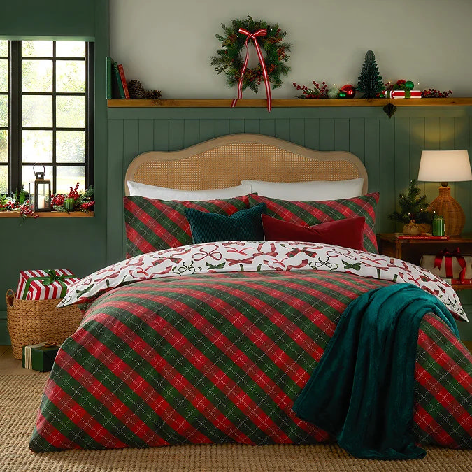 Red and green tartan Christmas bedding with festive bow print reverse, styled with velvet cushions and seasonal decorations