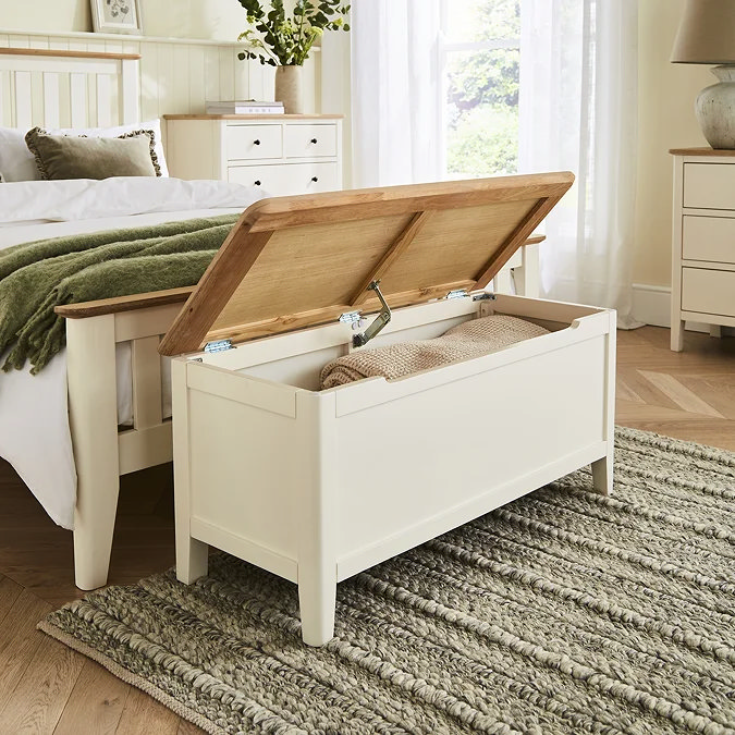 White painted wooden ottoman with oak lid used for toy and blanket storage in a bright bedroom.