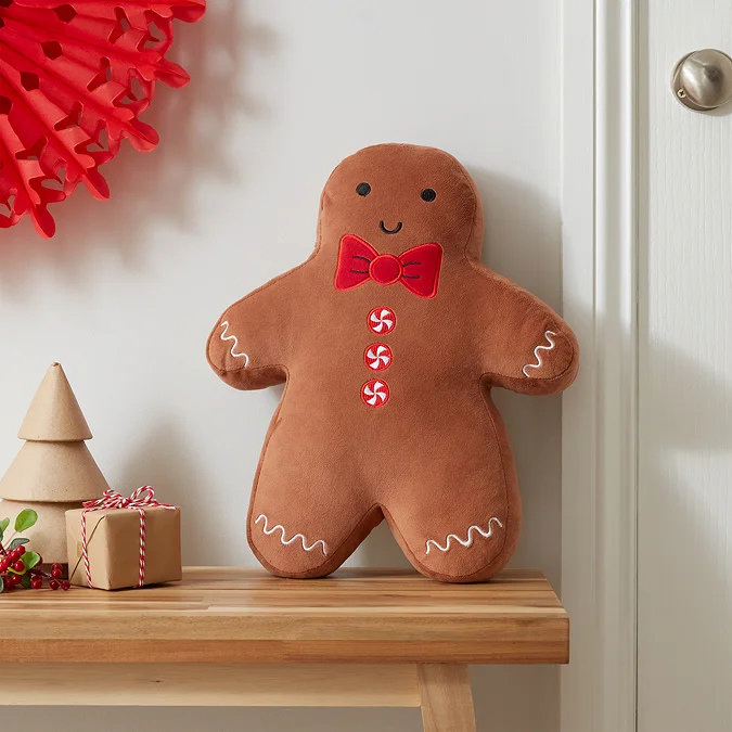 Gingerbread man shaped Christmas cushion with red bow tie and candy buttons on wooden bench