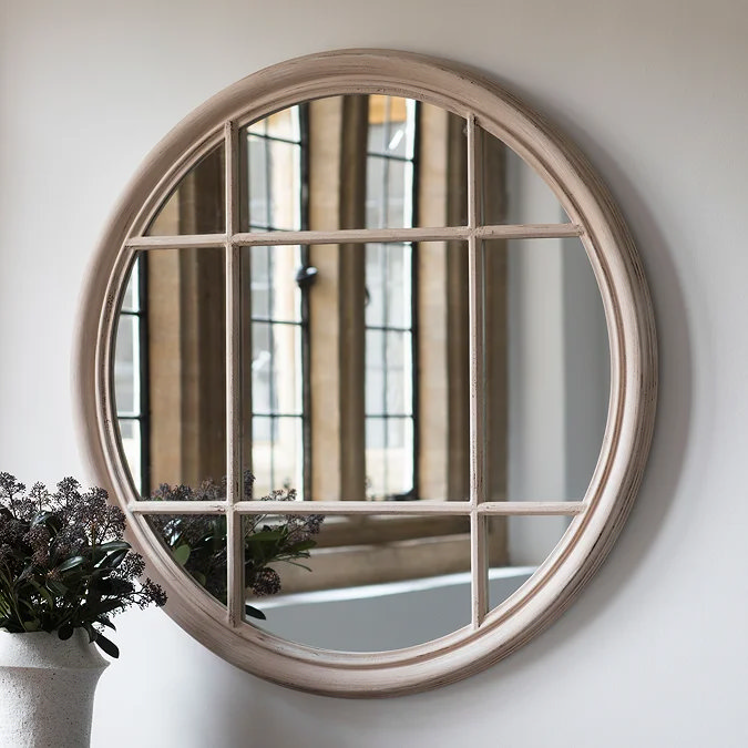 Round panelled wall mirror with distressed wooden frame, windowpane design adding vintage character to a living room wall.