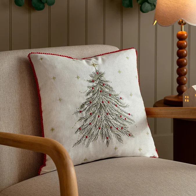Festive Christmas cushion with embroidered tree and red berries on beige chair in cosy bedroom corner