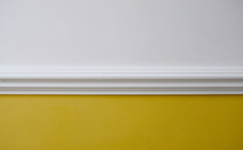 Two-tone dado paint trick for a narrow hallway—mustard yellow below a white dado rail with white upper walls—adds a widening horizontal line.