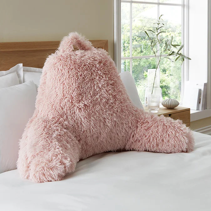 Pink faux fur cuddle cushion on bed