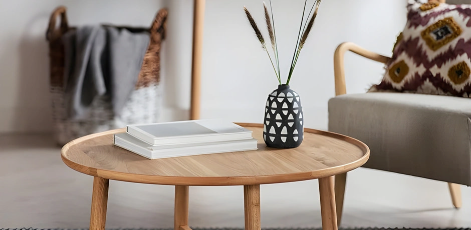 Round wooden coffee table styled with stacked books and a simple vase, creating a relaxed Scandi style living room look