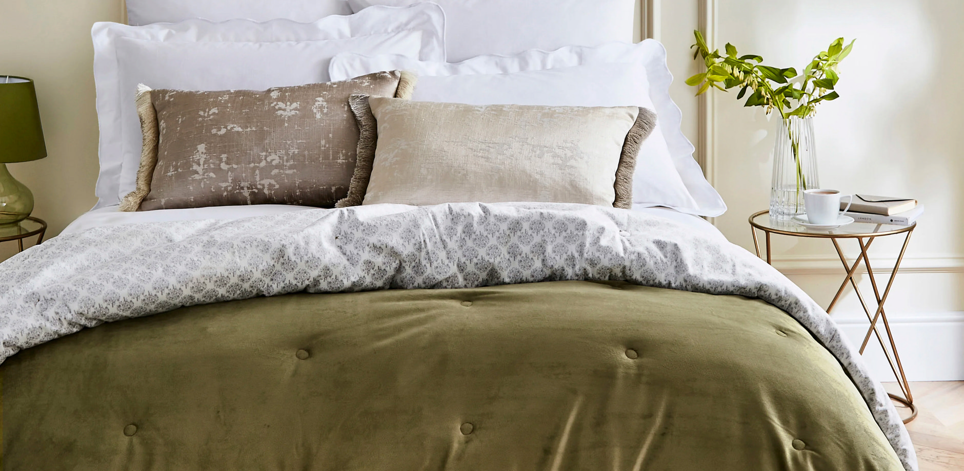 Freshly made bed with a green bedspread, white bedding and layered cushions – example of a clean bedspread after washing.