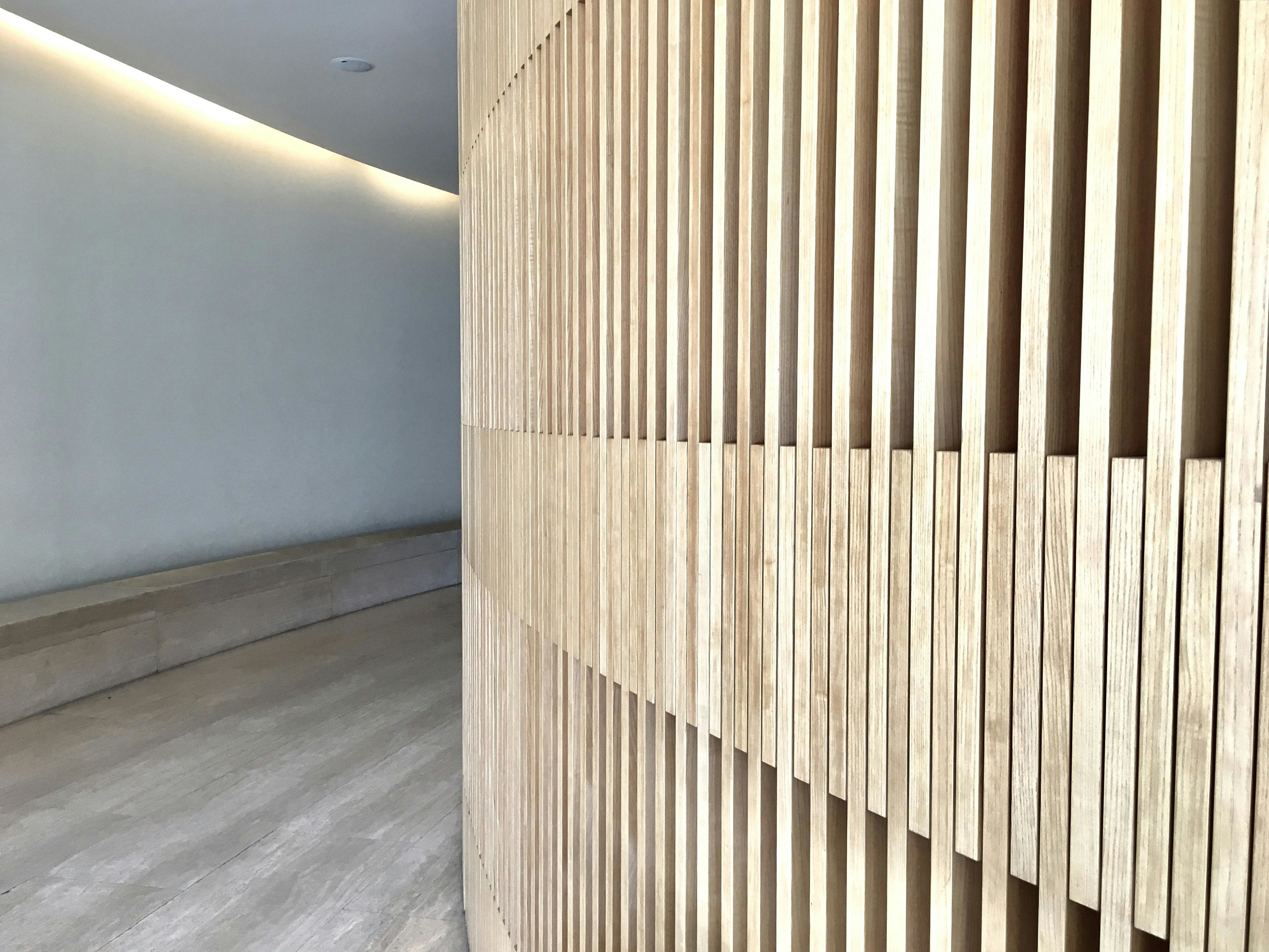 Modern hallway with vertical wood slat feature wall and concealed LED cove lighting washing the opposite wall—textures that add depth and make a narrow hall look wider.