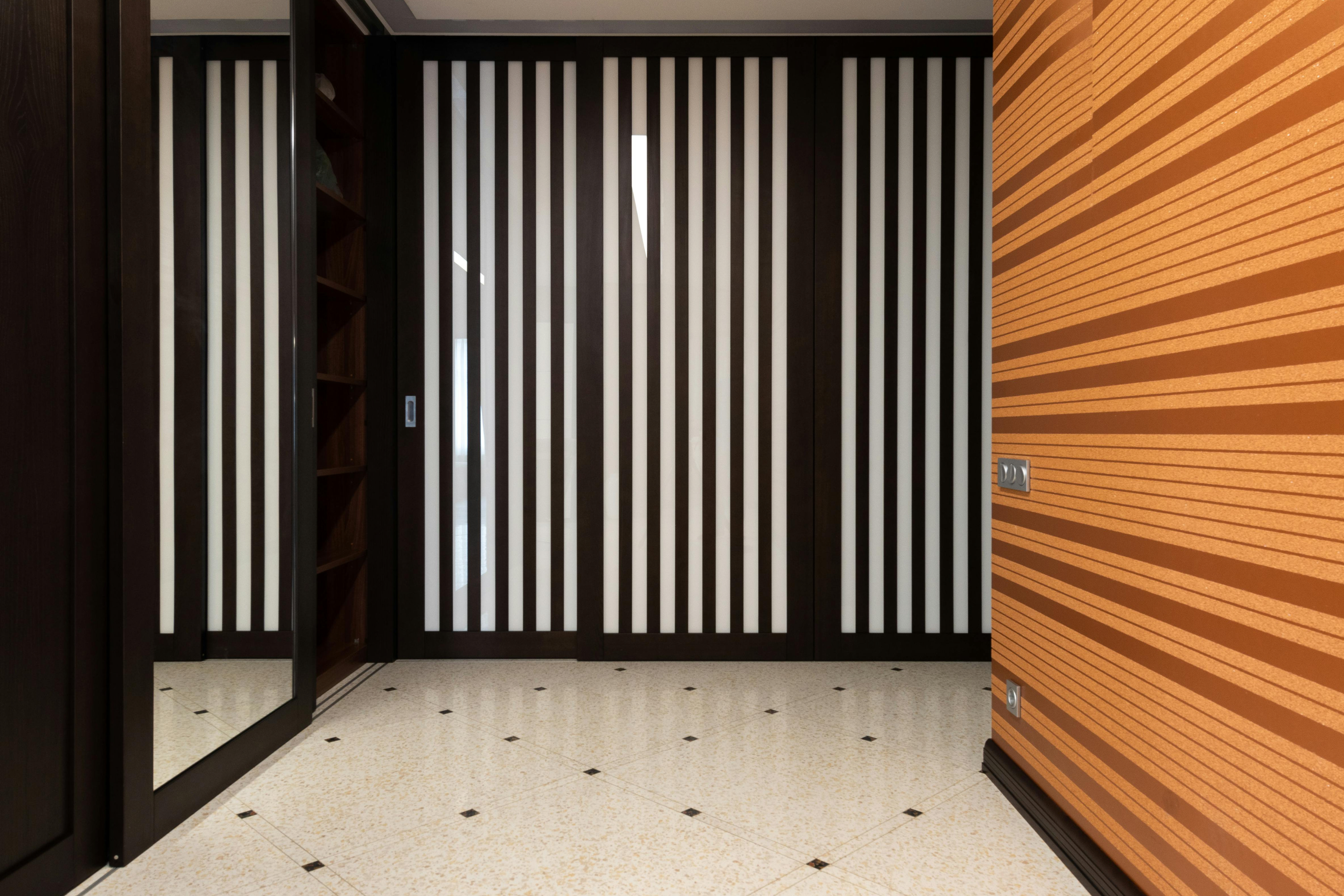 Narrow hallway with a horizontal striped feature wall and mirrored wardrobe; stripes make the corridor look wider while vertical slatted doors add height.